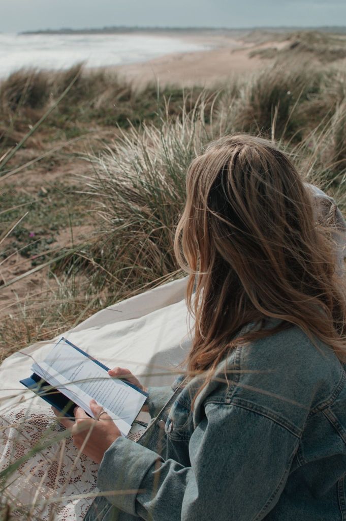 Woman gazing out to sea with an open book in her hands.