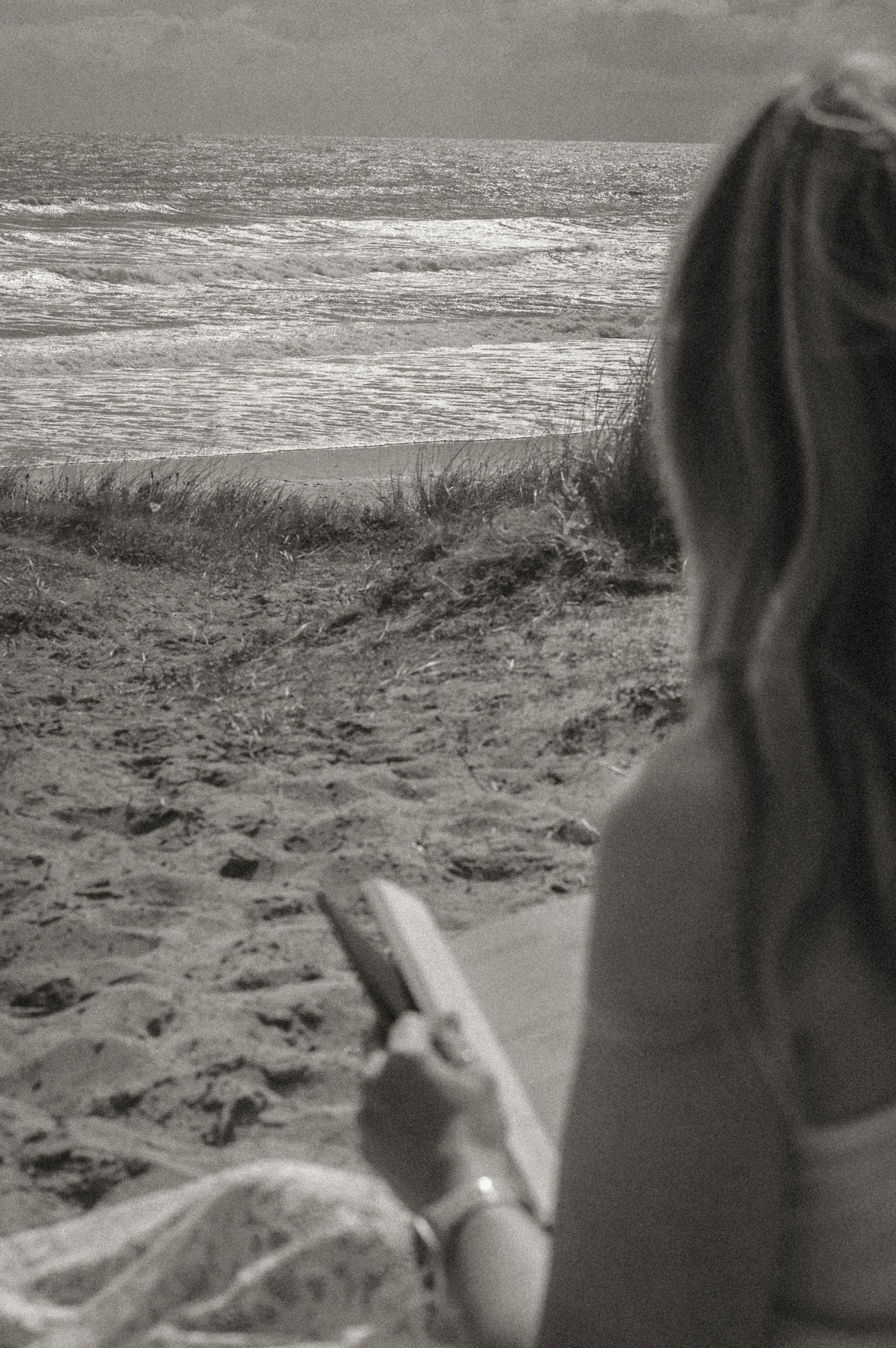 Woman sitting on the beach facing the sea looking at a book