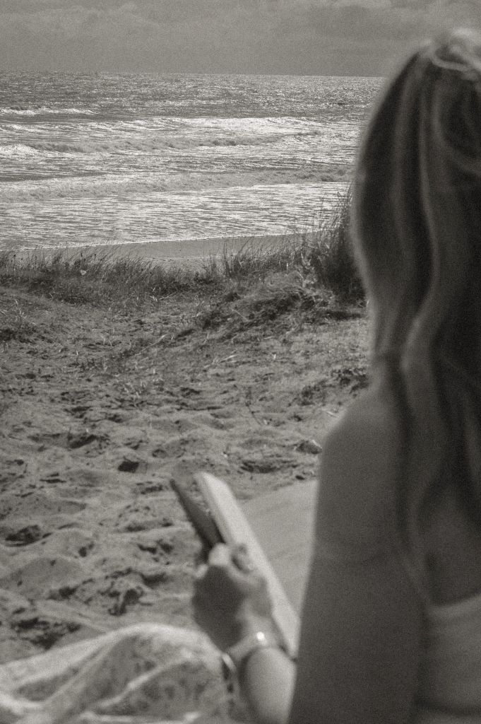 Woman sitting on the dunes reading facing towards the sea.