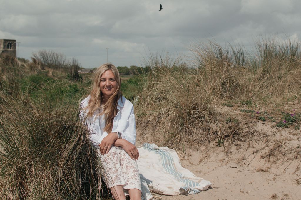 Woman sitting on sand smiling at camera. Text on the image says 'I write content that turns browsers into buyers' .