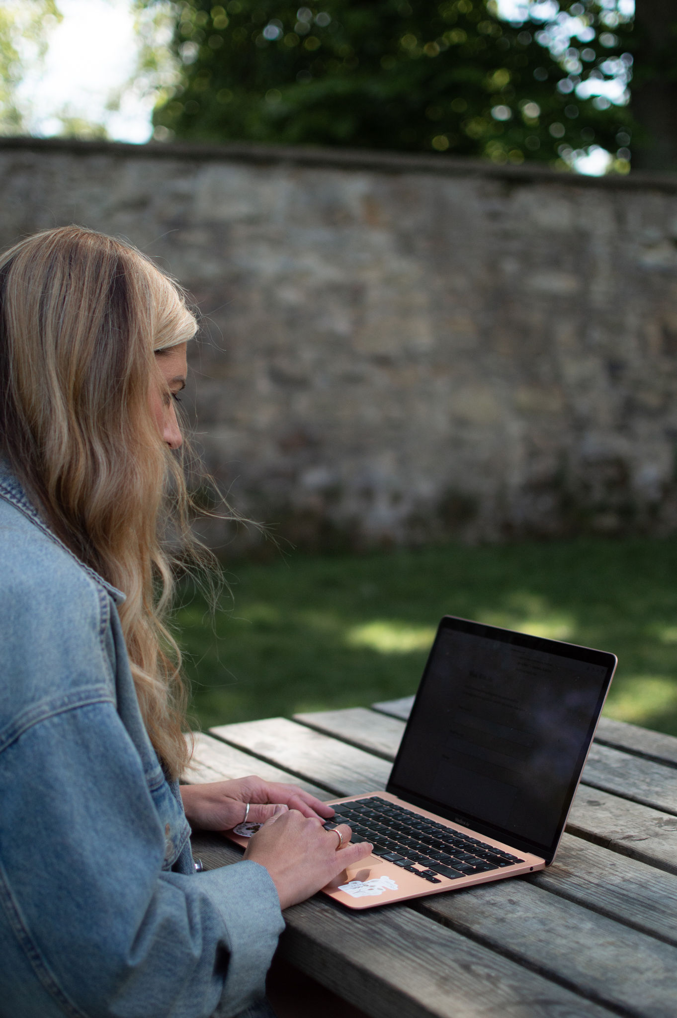 Copywriter sitting at a picnic table writing blog posts on her laptop