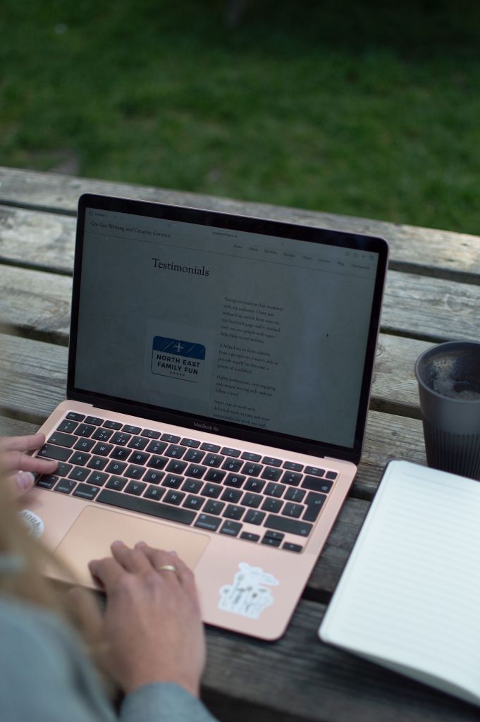 Laptop open on a table in a garden. The screen on the laptop displays a 'Testimonials' page.