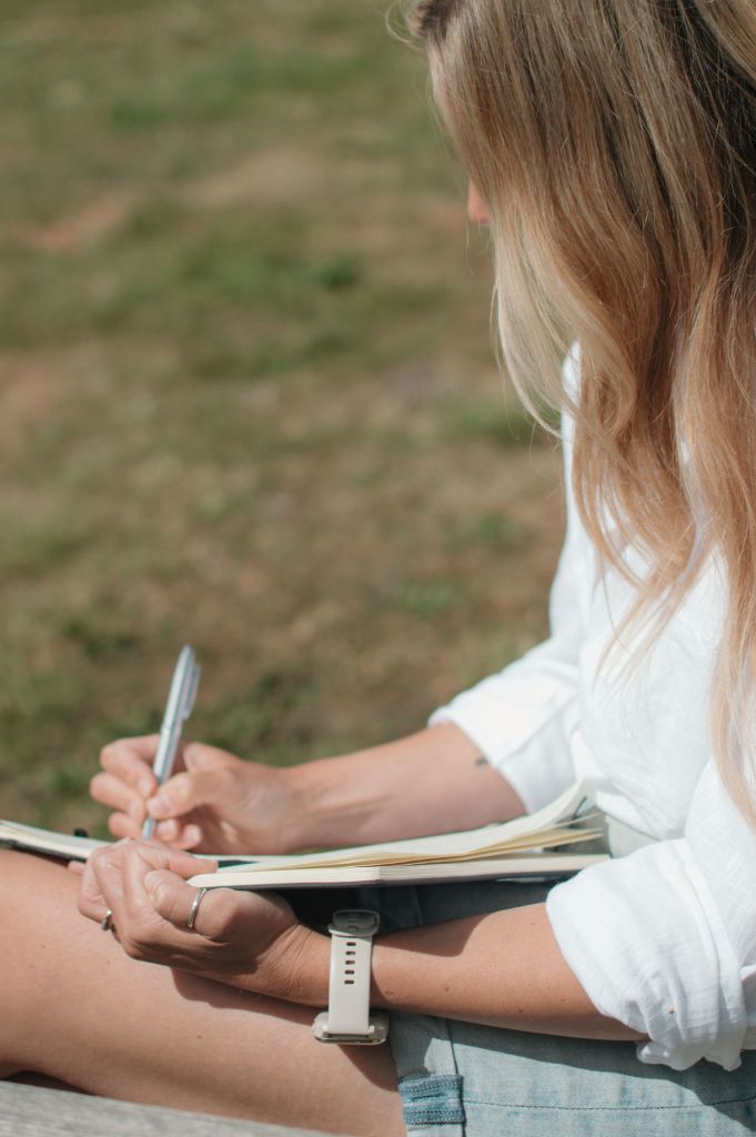 Woman sitting on grass writing in a notebook.