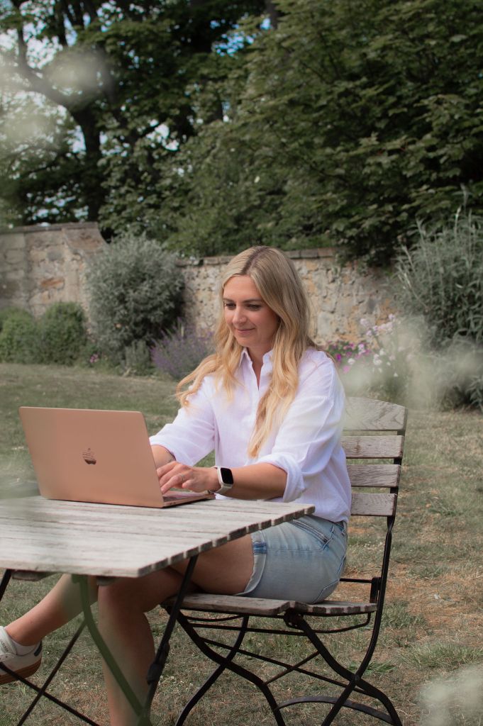 Woman sat at a table outside, looking at her laptop as she types.