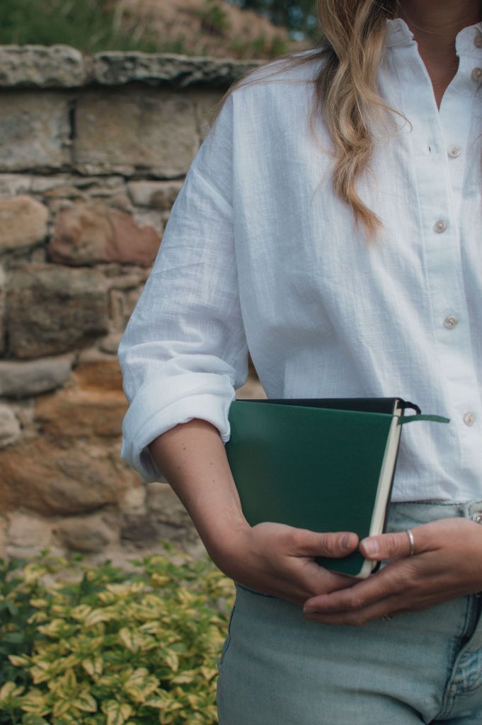Woman in white shirt and denim jeans holding a green and black notebook
