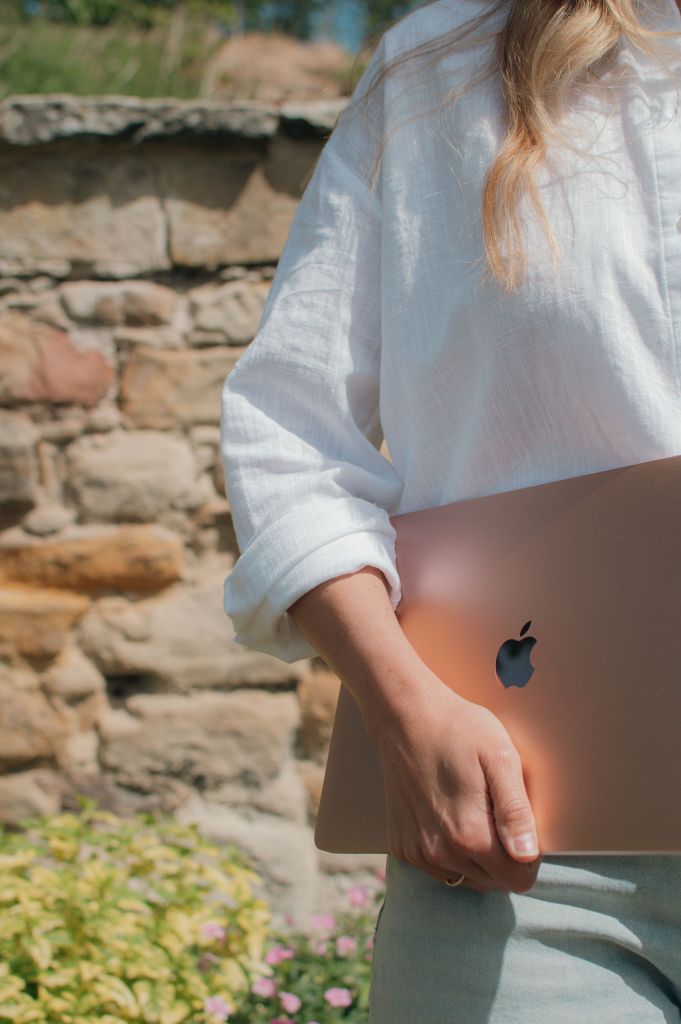 Woman's arm holding a laptop with a brick wall behind her
