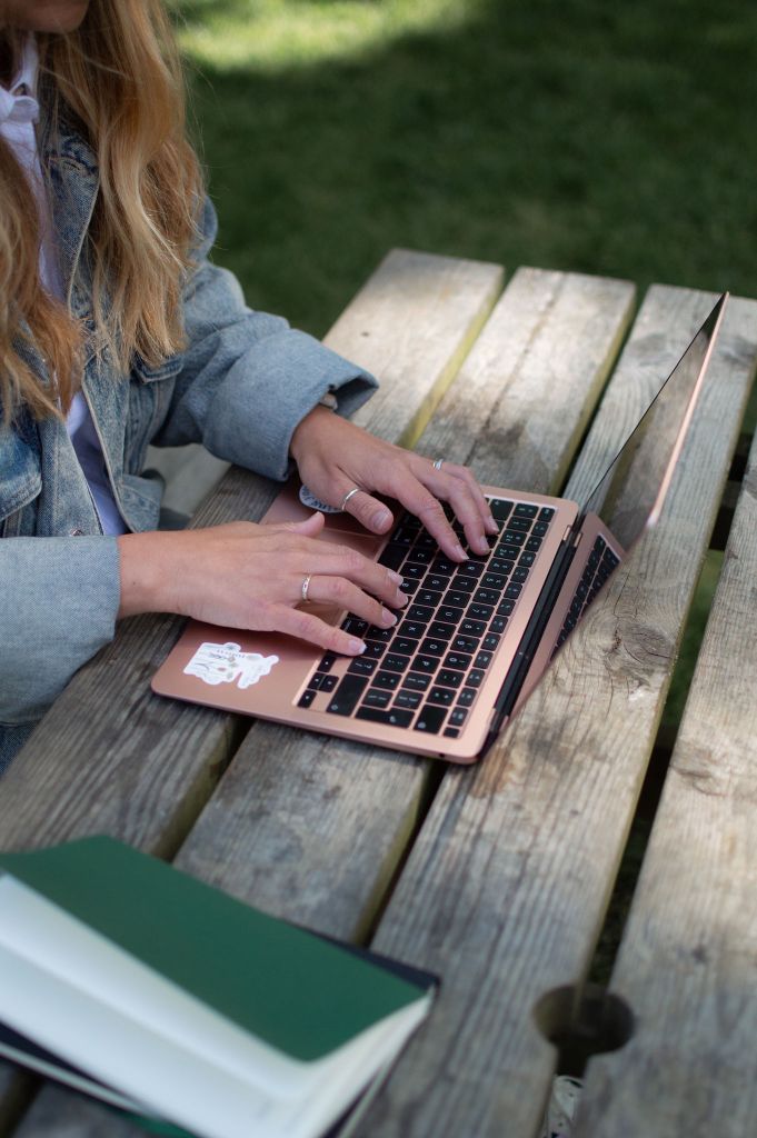 Woman typing on her laptop at a picnic table. The camera is focused on the laptop and her hands.
