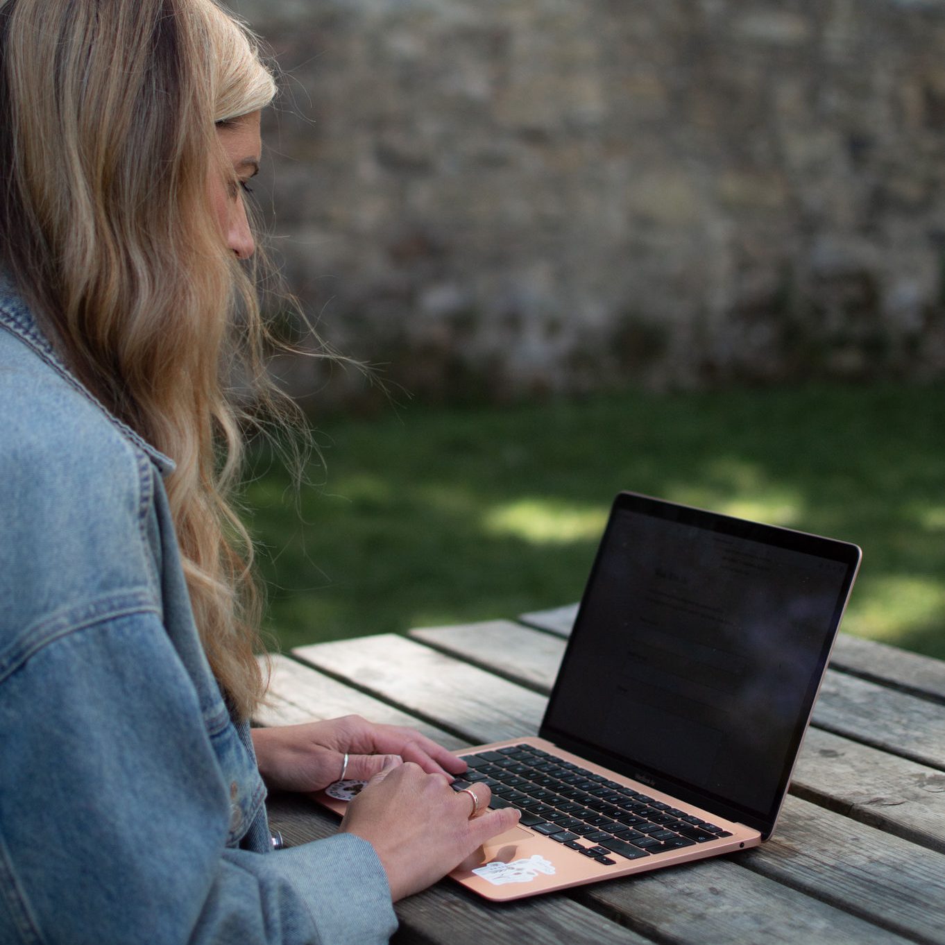 Copywriter sitting at a picnic table writing blog posts on her laptop