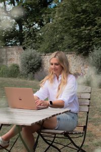 Woman sat at a table outside, looking at her laptop as she types.